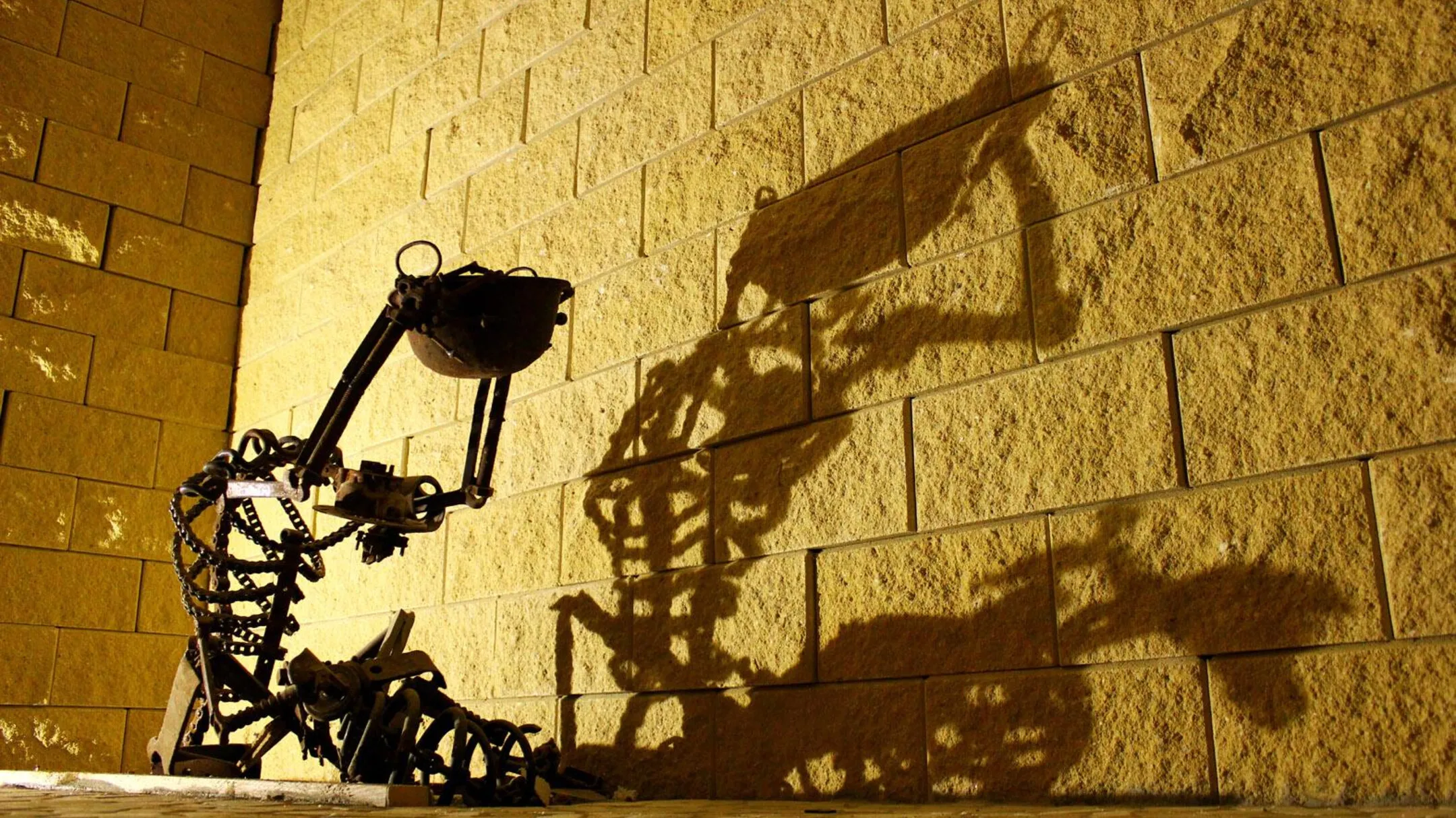 Metal sculpture made of mechanical parts casting a shadow of a figure on a textured stone wall