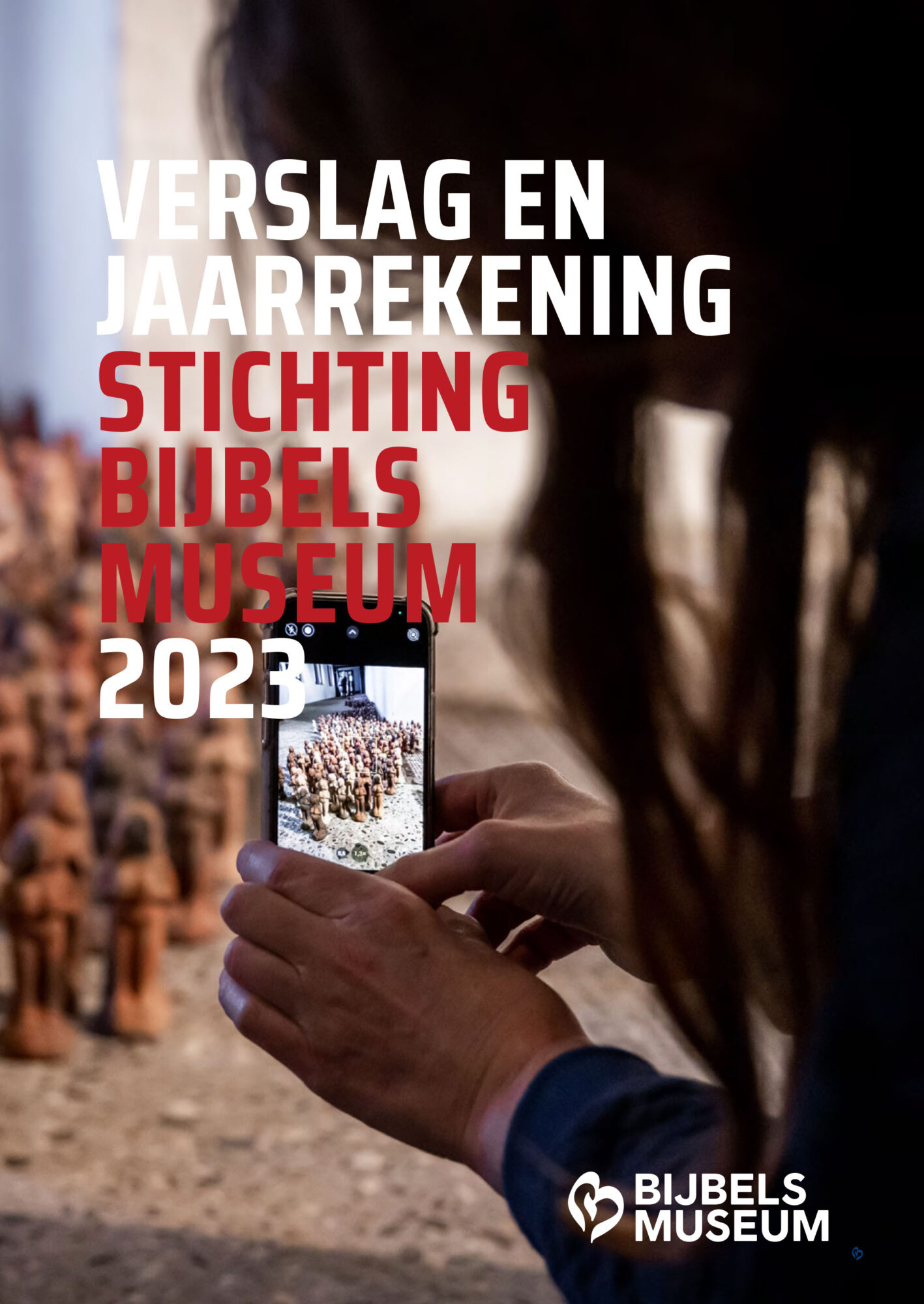 Jaarverslag 2023 Stichting Bijbels Museum, met op de omslag handen die een smartphone vasthouden om kleine beeldjes met het museumlogo te fotograferen