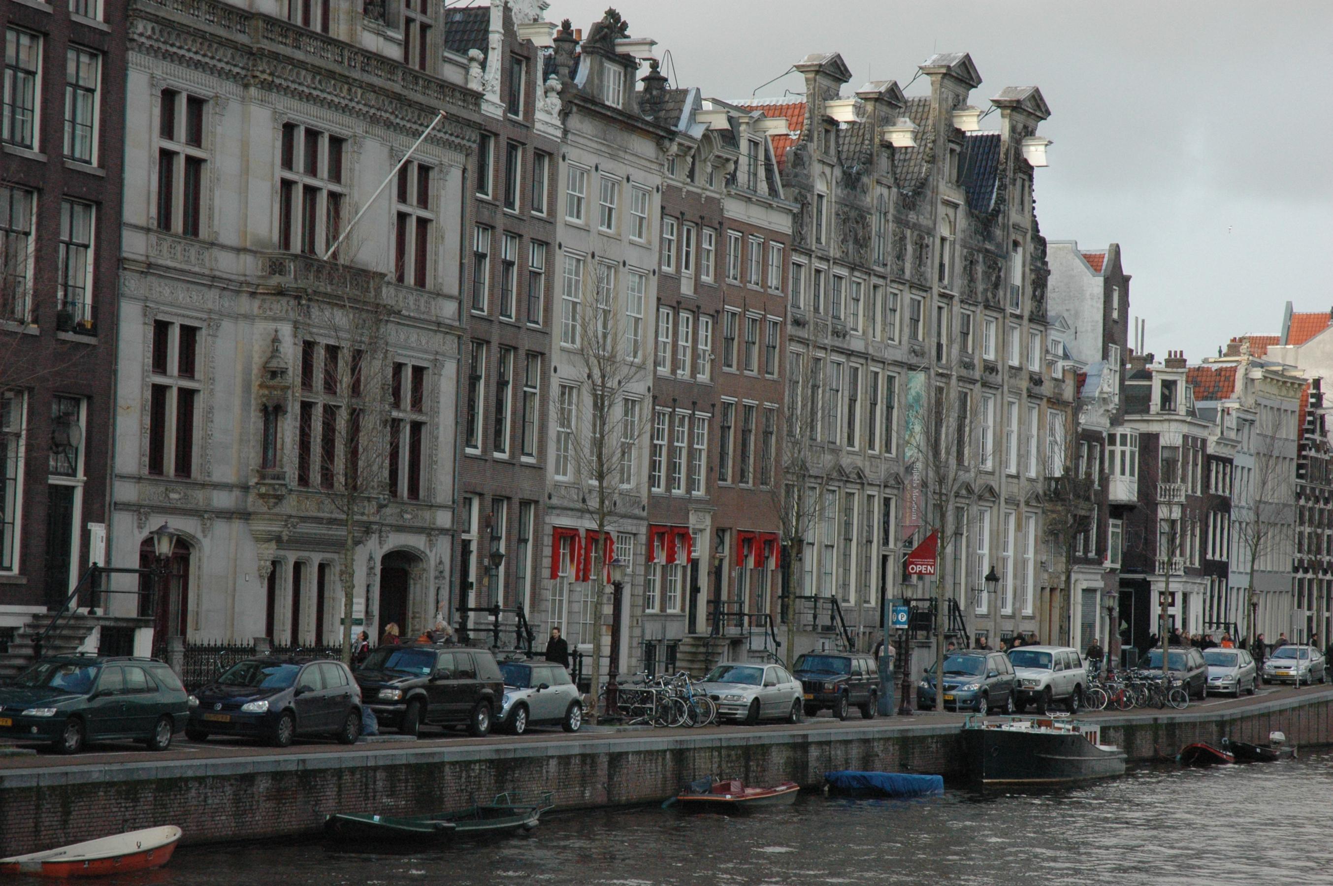 historische grachtenpanden langs een waterweg met geparkeerde auto's en boten