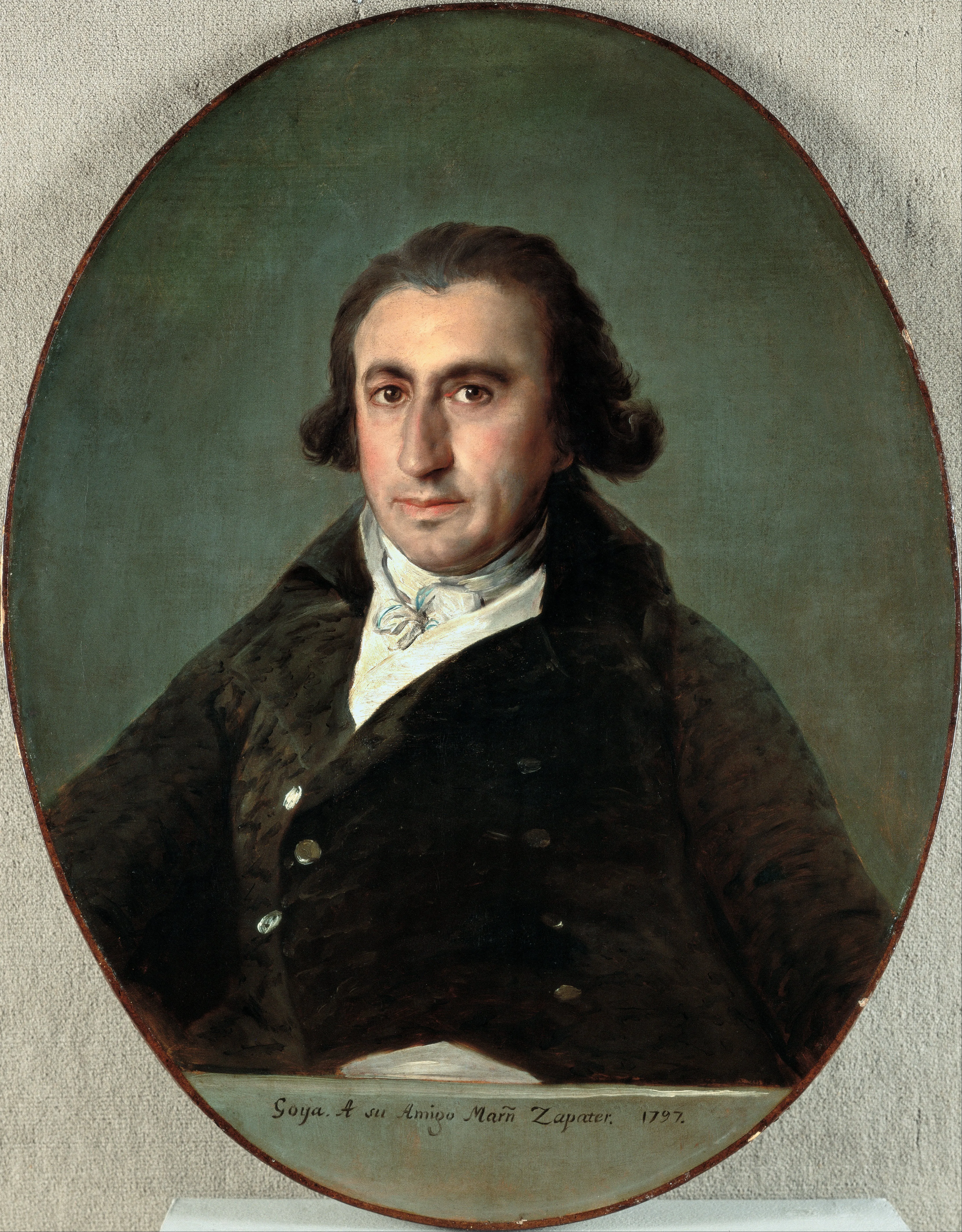Ovaal portret van een man met donker haar in een donkere jas en witte cravat tegen een gedempte groene achtergrond, met onderaan de inscriptie 'Goya A su Amigo Martín Zapater. 1797'