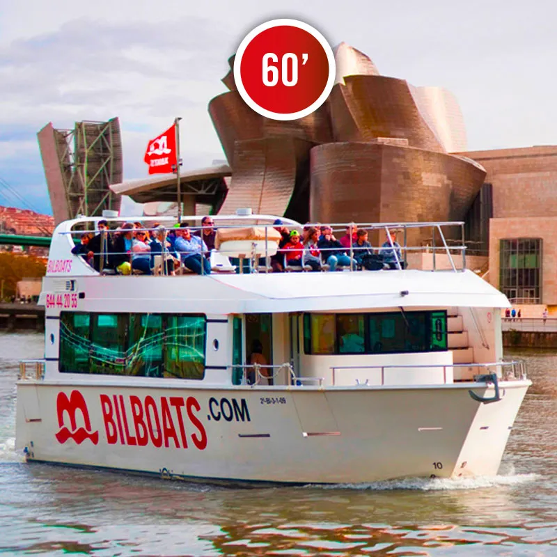 Biały statek wycieczkowy Bilboats z pasażerami na górnym pokładzie płynący rzeką Nervión w Bilbao, z widocznym w tle Muzeum Guggenheima w Bilbao.