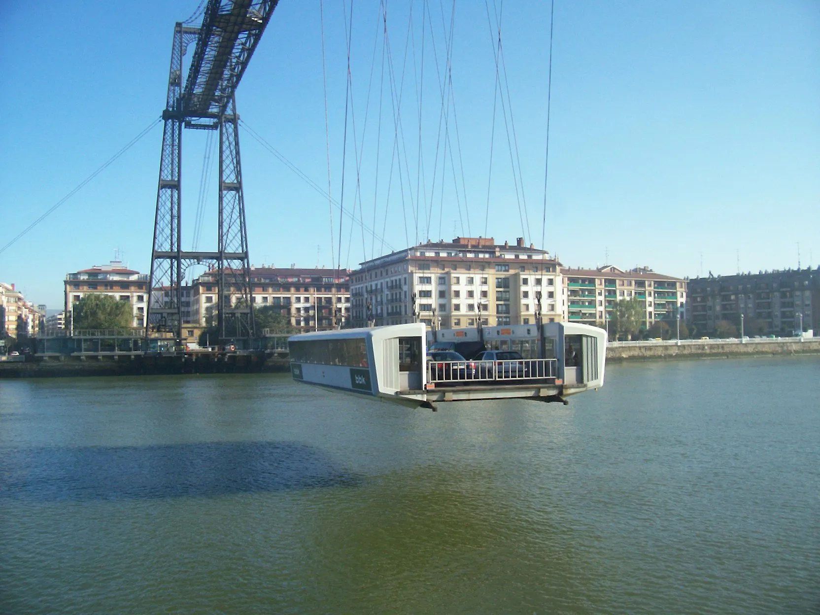 La barquilla suspendida del Puente de Bizkaia cruzando la ría, con una torre de celosía de hierro y edificios frente al agua al fondo