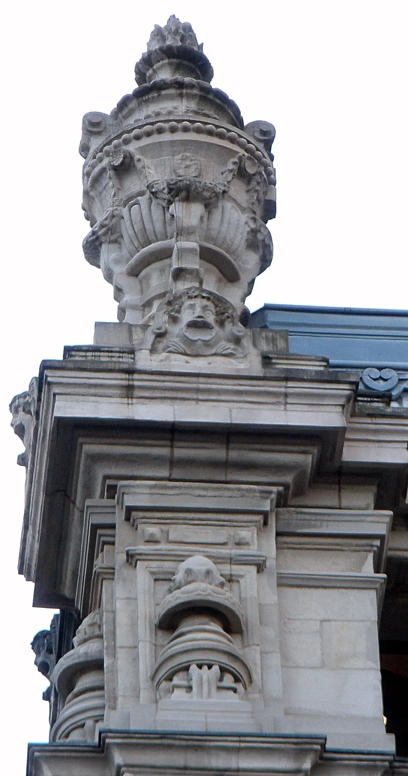 Ornate stone finial with decorative urn and mascaron face atop a pilaster of an eclectic civic building