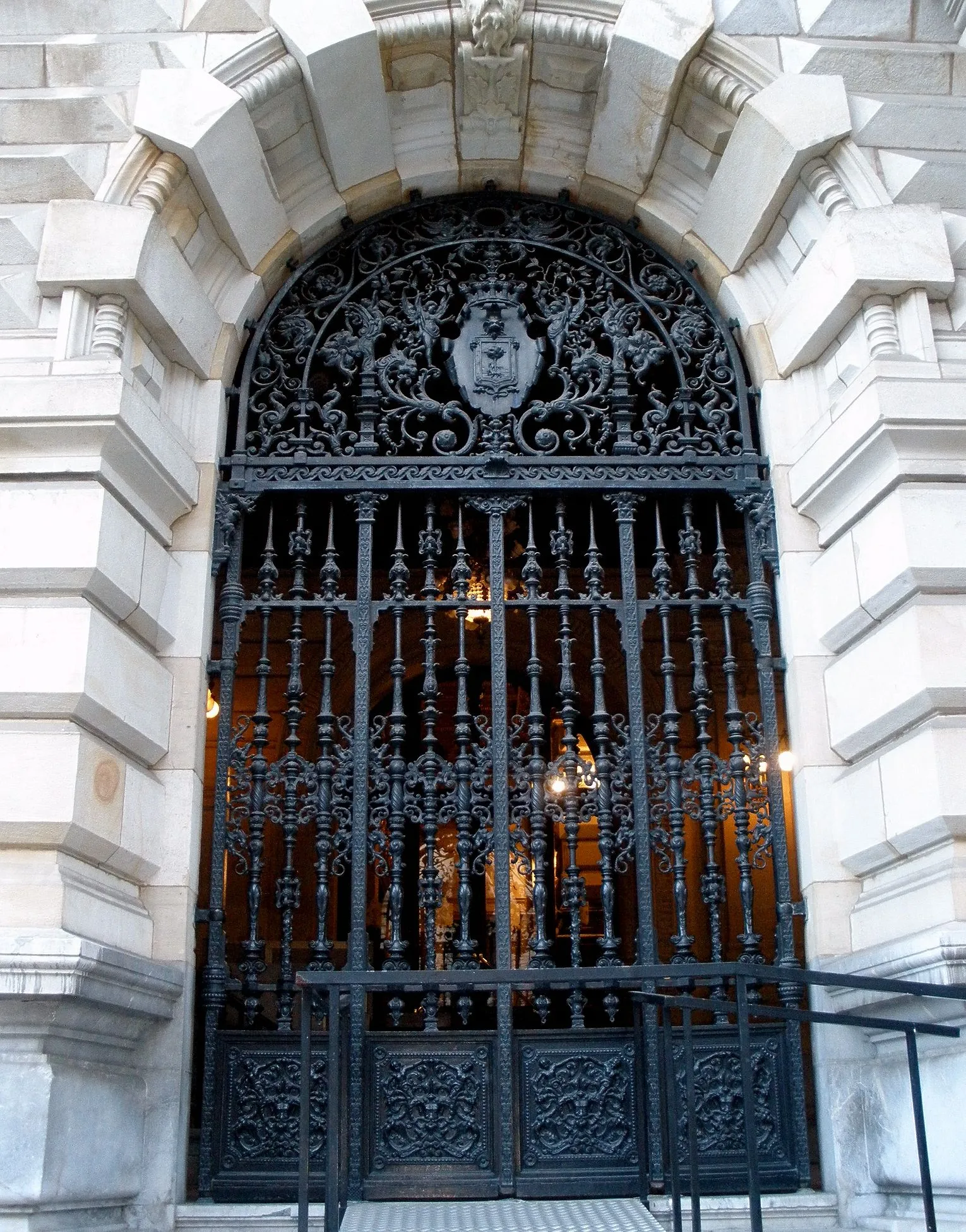 A large ornate black iron gate with a coat of arms set within a stone archway at the entrance of a building.