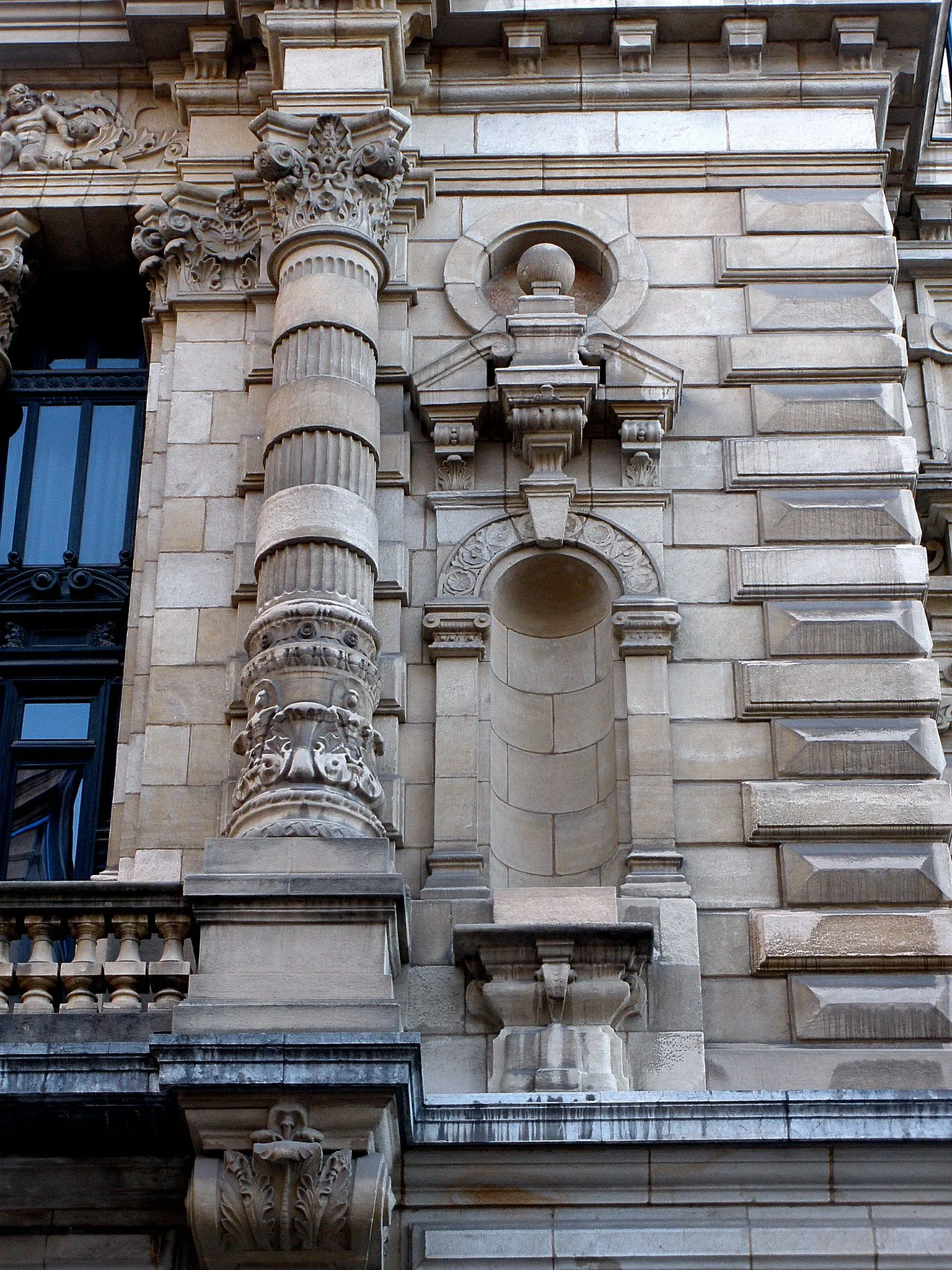 Close-up of the ornate stone facade of the Bizkaia Provincial Council Palace, showing a fluted column with decorative capital, arched niches, and rusticated masonry.