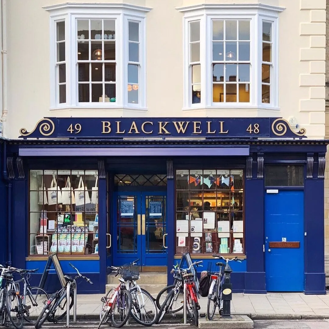 Niebieska fasada witryny Blackwell's Bookshop ze złotym napisem '49 BLACKWELL 48', dużymi oknami wystawowymi z książkami i torbami prezentowymi oraz rowerami zaparkowanymi na chodniku