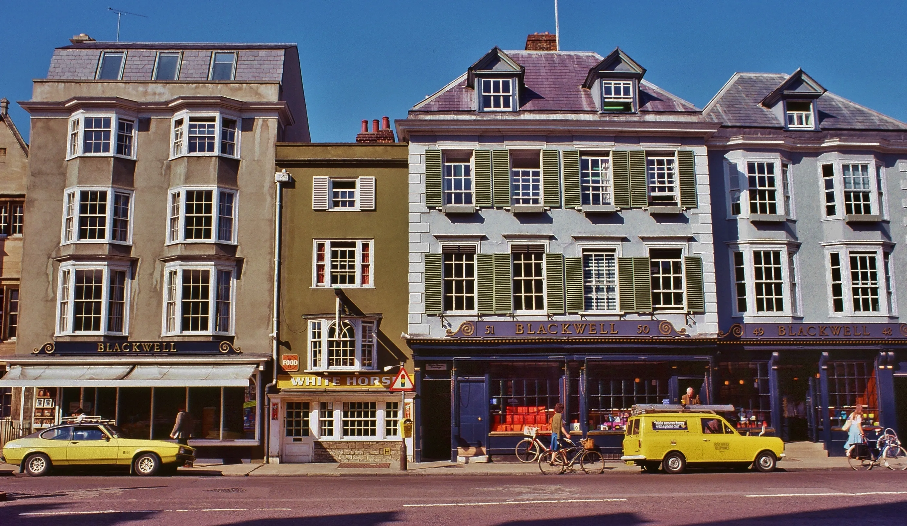 Widok ulicy na Blackwell's Bookshop i sąsiednie budynki przy Broad Street w Oksfordzie, z zabytkowymi żółtymi samochodami zaparkowanymi na zewnątrz, wrzesień 1977 r.