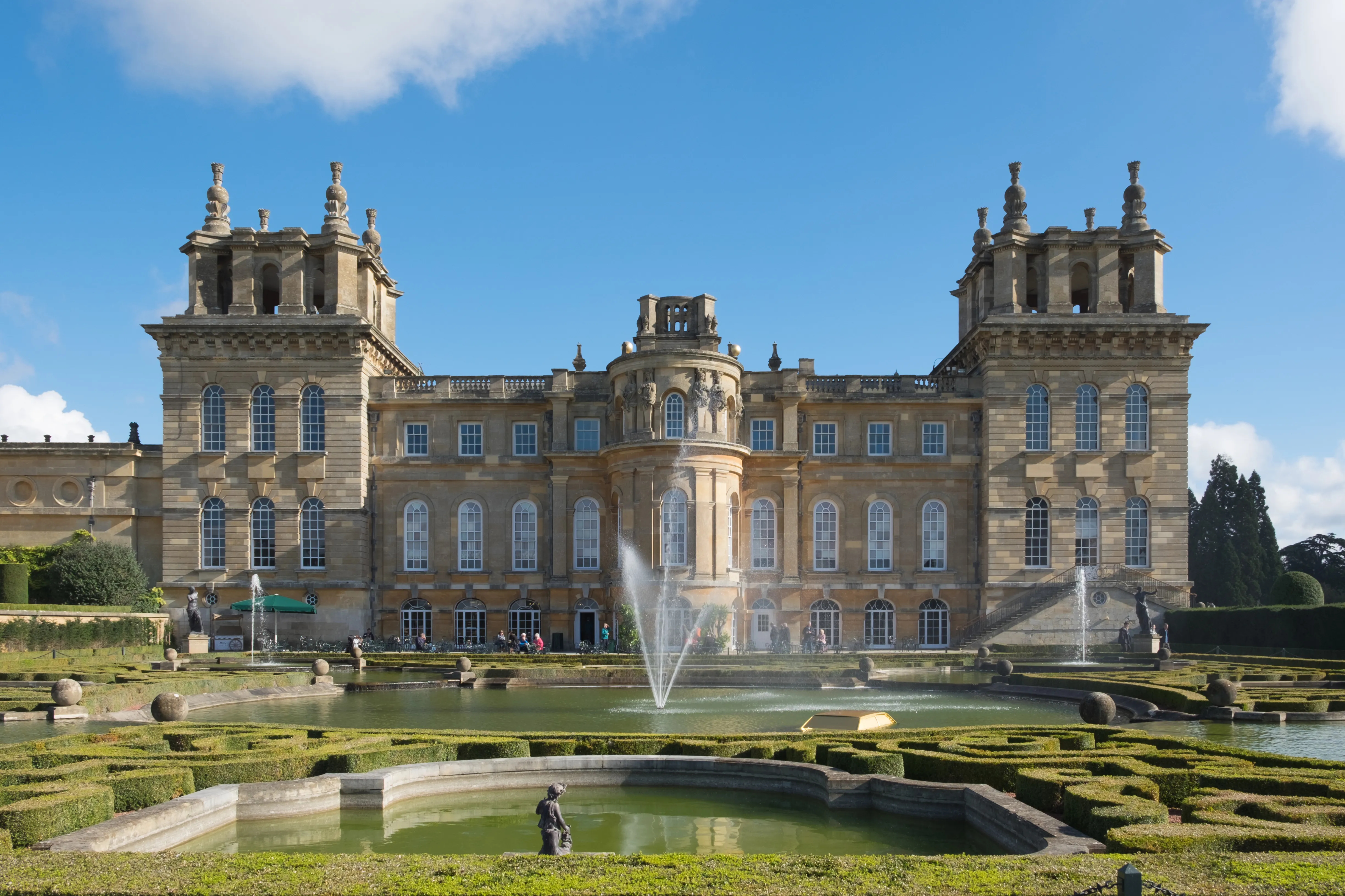 Fasada Blenheim Palace widziana od strony Water Terraces, z fontannami i ogłoszonymi ogrodami na pierwszym planie pod błękitnym niebem
