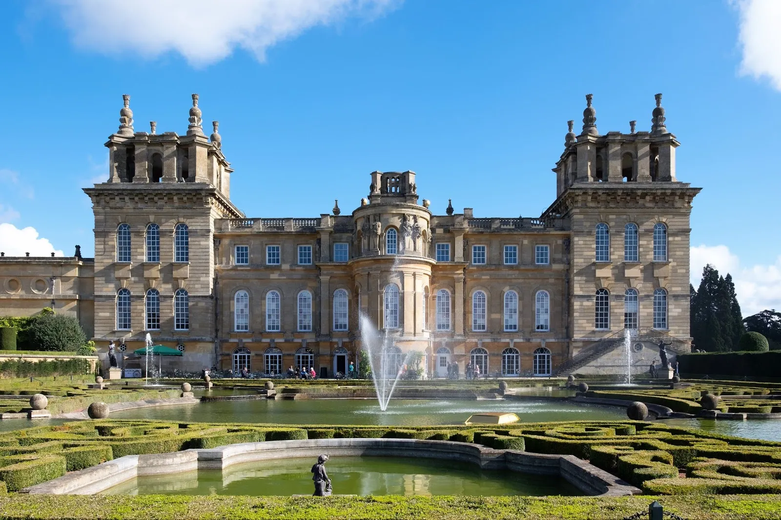 Blenheim Palace, okazały barokowy kamienny budynek z dwiema narożnymi wieżami, centralnym ryzalitem oraz fontanną w ogrodach formalnych przed wejściem