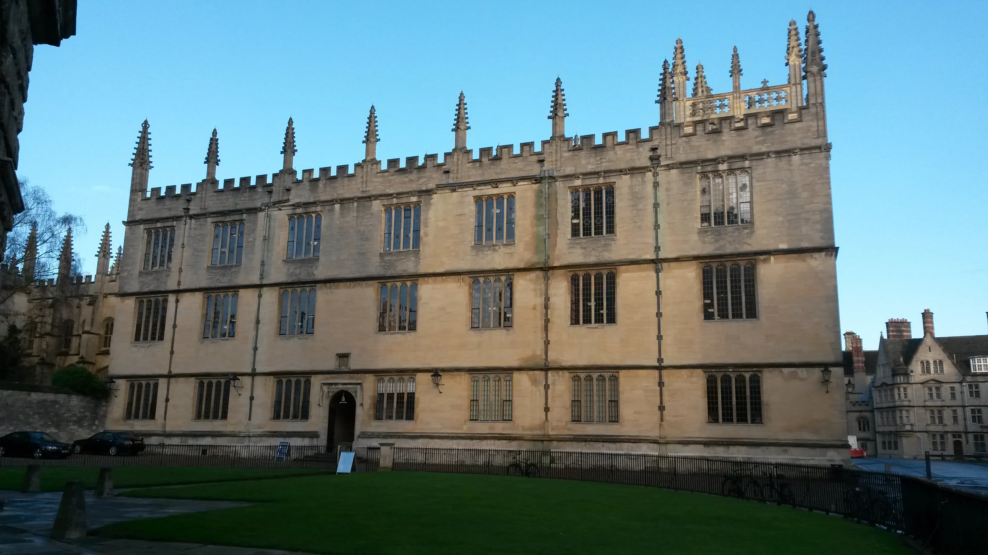 Fachada de piedra de la Bodleian Library con pináculos y almenas góticas, vista desde Radcliffe Square con un césped verde en primer plano