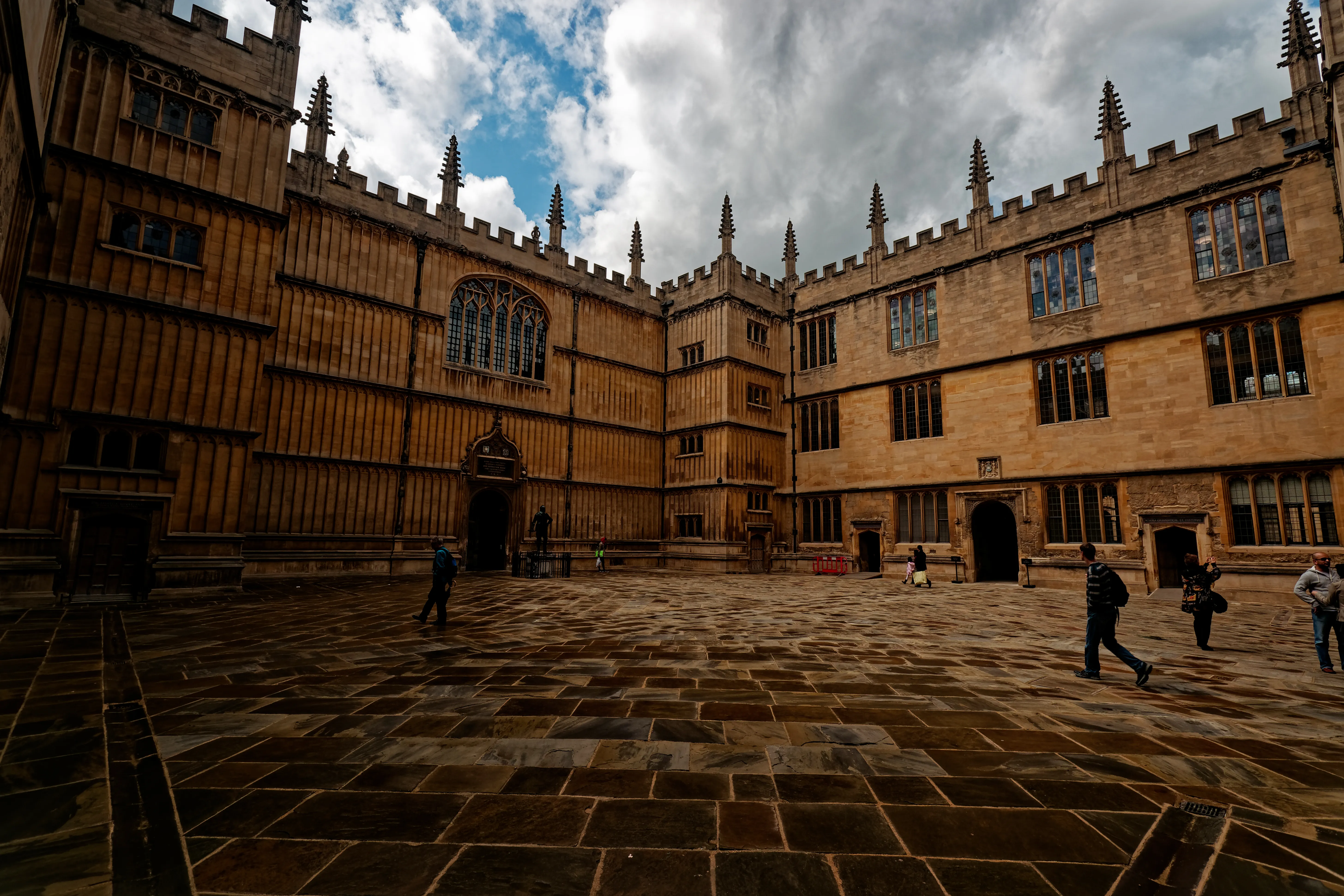 Patio empedrado del Old Schools Quadrangle de la Bodleian Library con fachada de piedra gótica, pináculos y visitantes caminando.