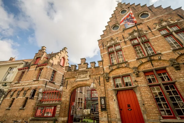 Vista en ángulo contrapicado de la histórica fachada de ladrillo de la cervecería Bourgogne des Flandres, que presenta hastiales escalonados, puertas rojas y una bandera ondeando sobre la entrada.