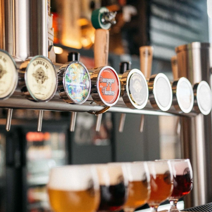 Hilera de tiradores de cerveza, incluyendo uno de Bourgogne des Flandres, sobre una fila de vasos de degustación llenos de cervezas de diversos tonos ámbar y oscuros