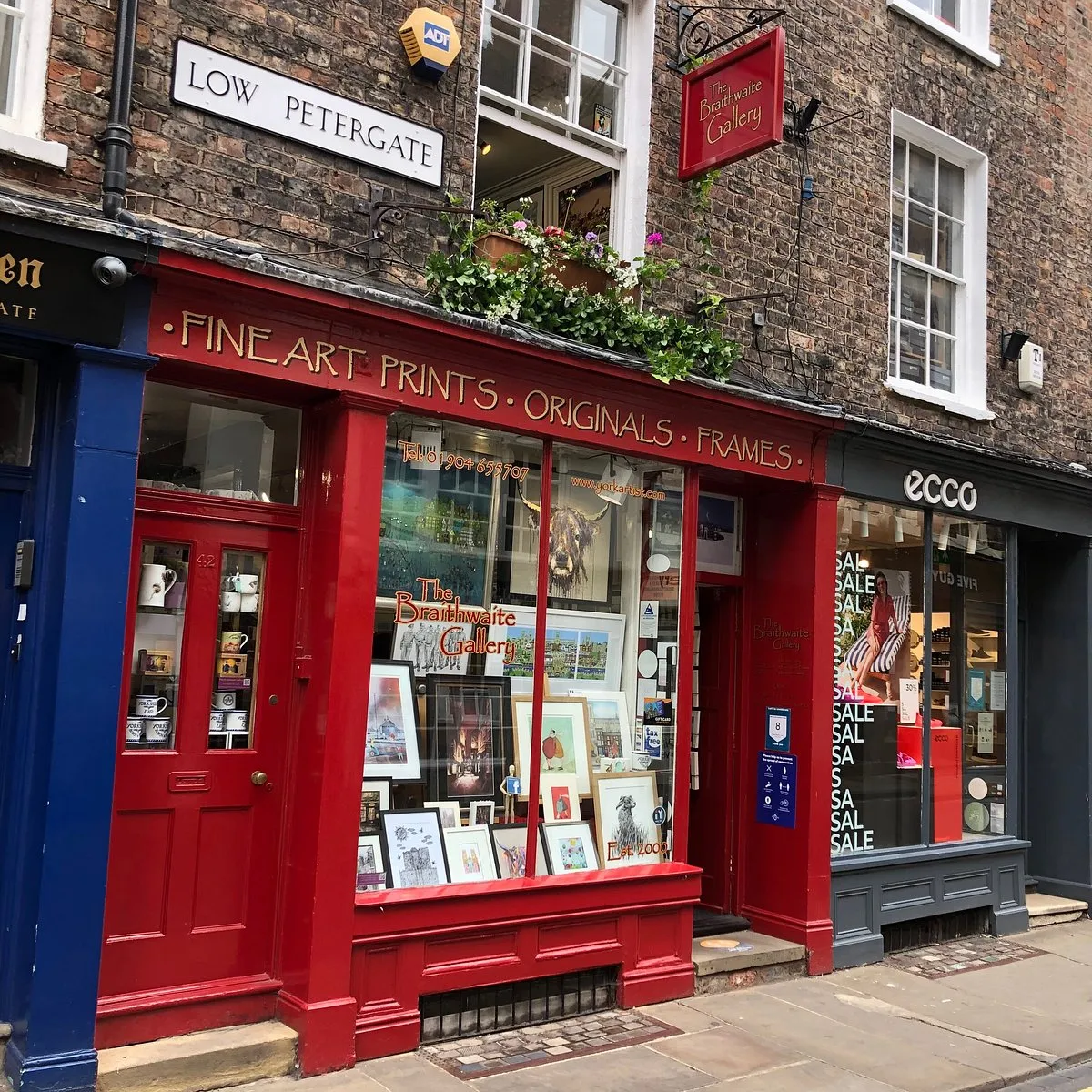 Red-painted storefront of The Braithwaite Gallery on Low Petergate, with large display windows showing framed artworks and a hanging sign reading Braithwaite Gallery