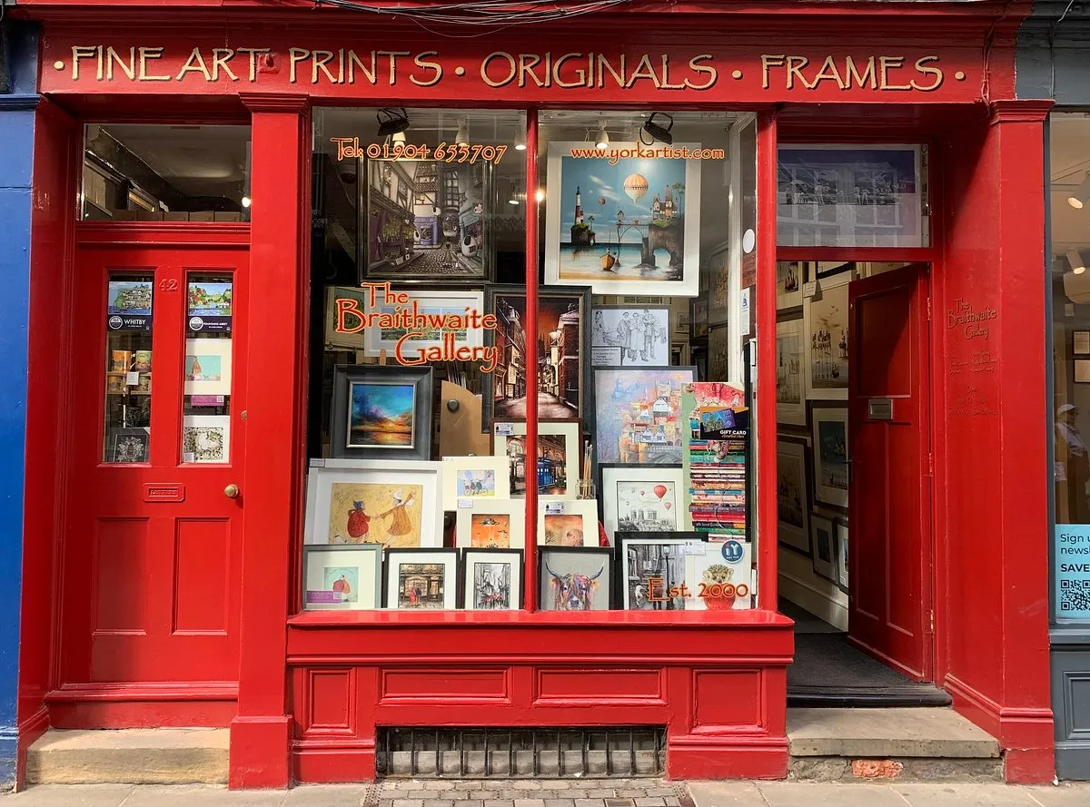 Bright red storefront of The Braithwaite Gallery with framed artworks displayed in the window and gold signage reading Fine Art Prints Originals Frames