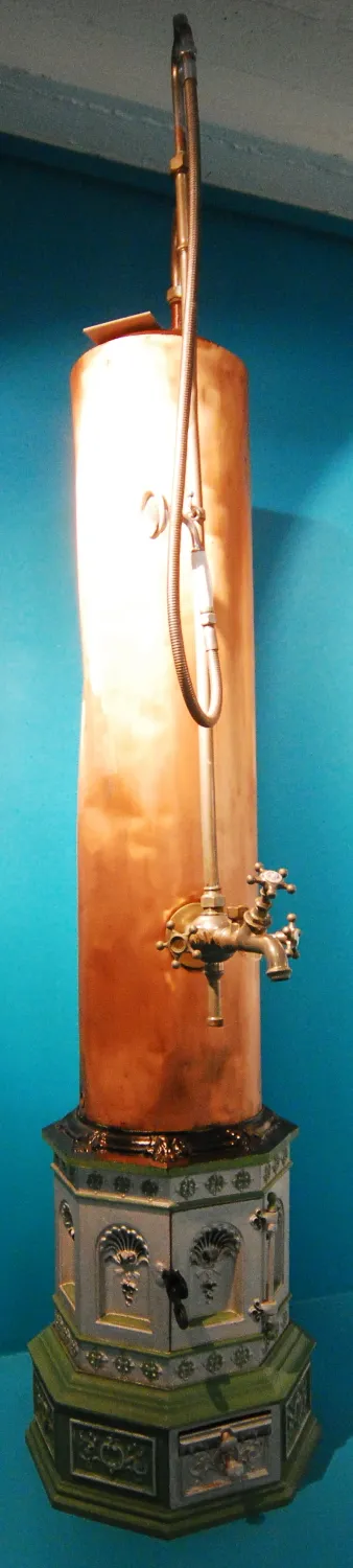 Un alto aparato de calefacción de cobre con una base decorativa y accesorios de latón contra una pared azul