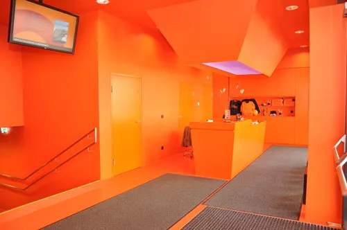 Interior de un museo con paredes de color naranja brillante, un mostrador de recepción y una escalera