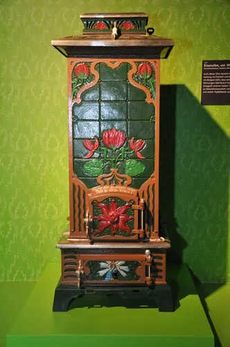 Estufa antigua ornamentada con azulejos florales rojos y fondo verde en exhibición