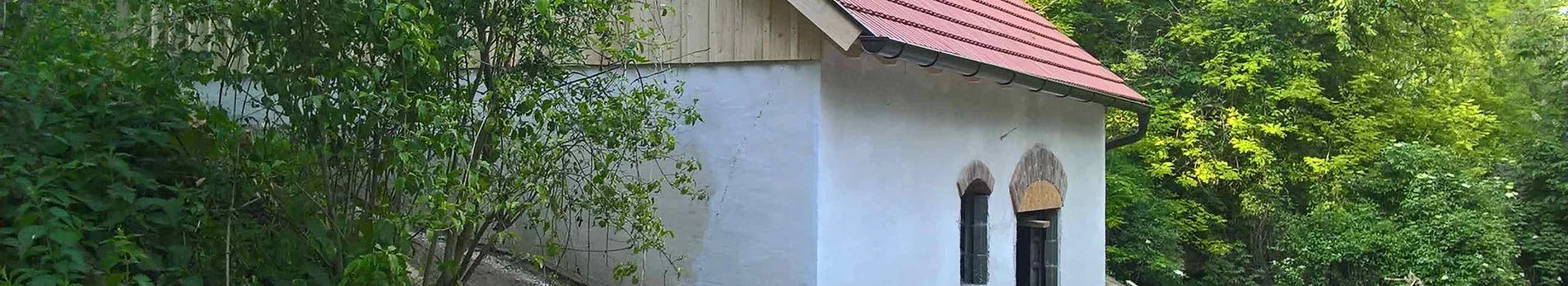 wit gebouw met rood dak en boogramen, omgeven door groene bomen