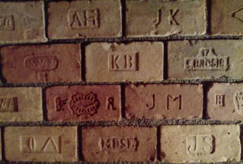 Close-up van een bakstenen muur met reliëfletters en logo's op individuele stenen