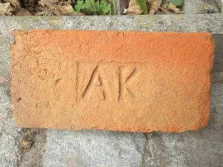 Close-up of a red brick with 'AK' stamped on it