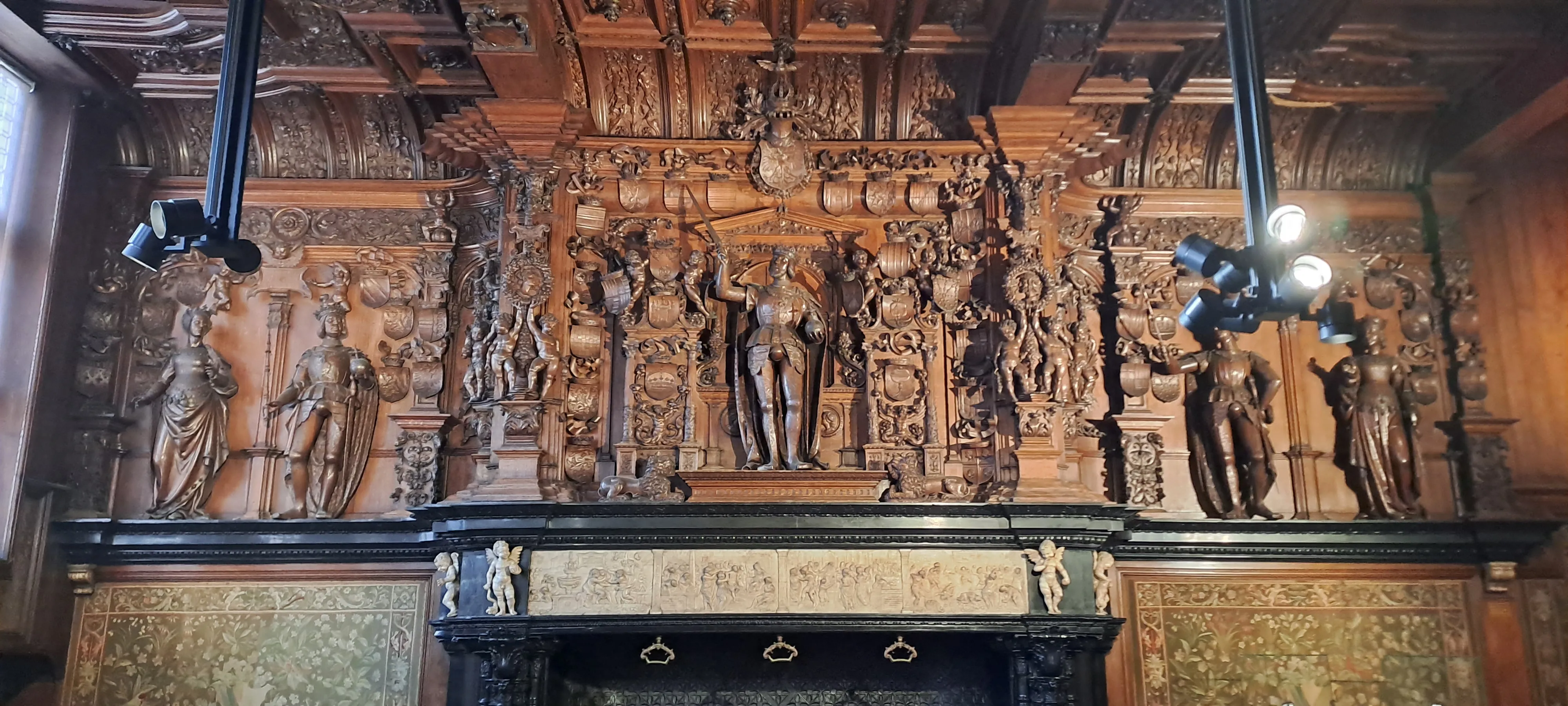 Chimenea de madera ornamentada con numerosas figuras esculpidas y paneles decorativos en la sala de los regidores del Brugse Vrije