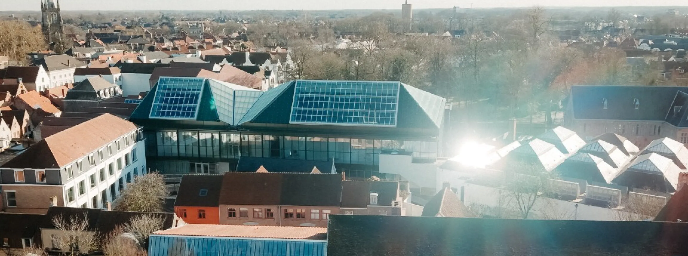 Vista aérea de un edificio moderno con un gran techo de cristal y paneles solares rodeado de tradicionales tejados de tejas rojas en Brujas