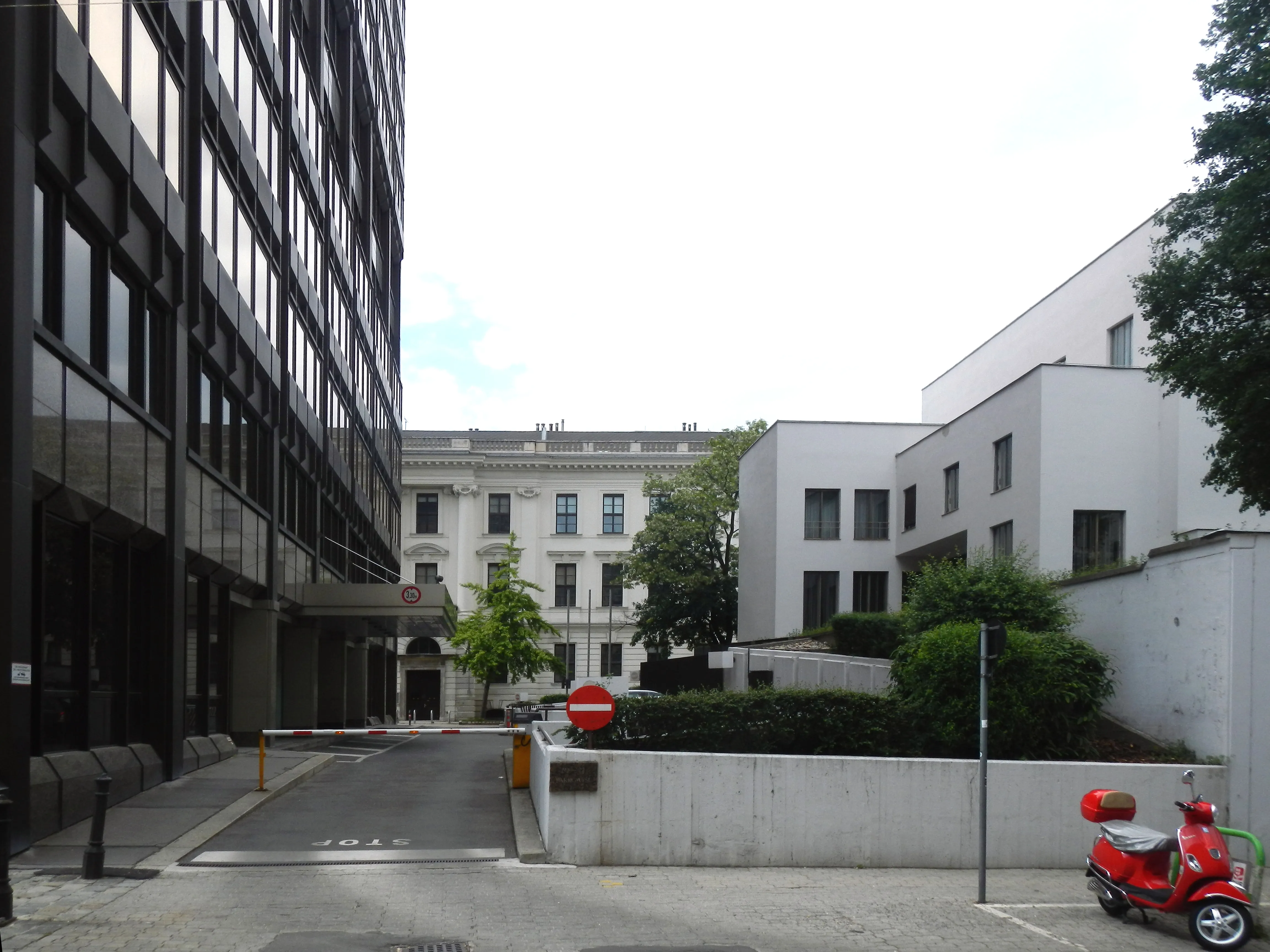 Een modern gebouw met een glazen gevel staat naast een wit gebouw in klassieke stijl met een rode scooter ervoor geparkeerd.