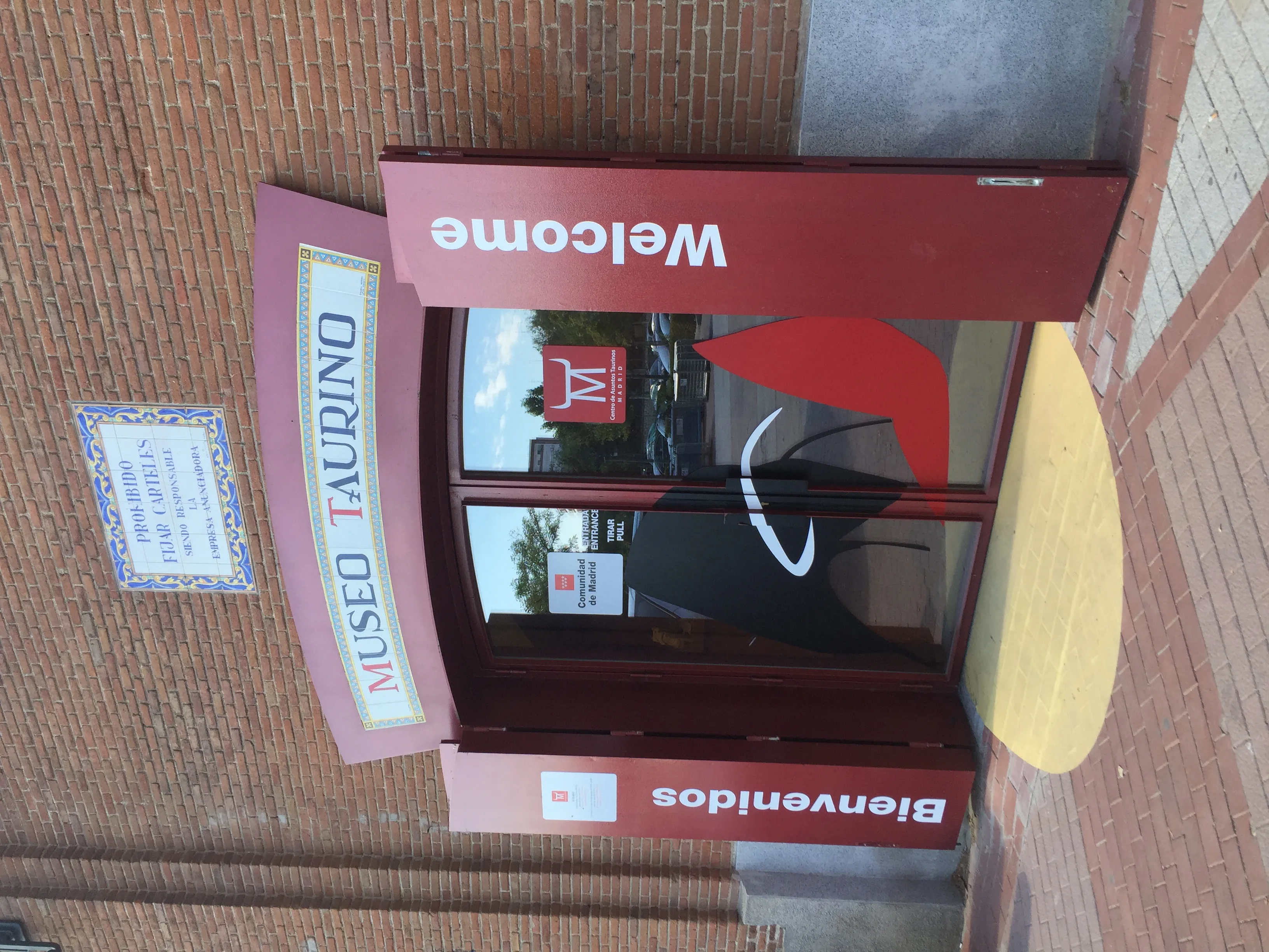 Señal de entrada roja para el Museo de Tauromaquia con el texto 'MUSEO TAURO' y 'Welcome' en un edificio de ladrillos
