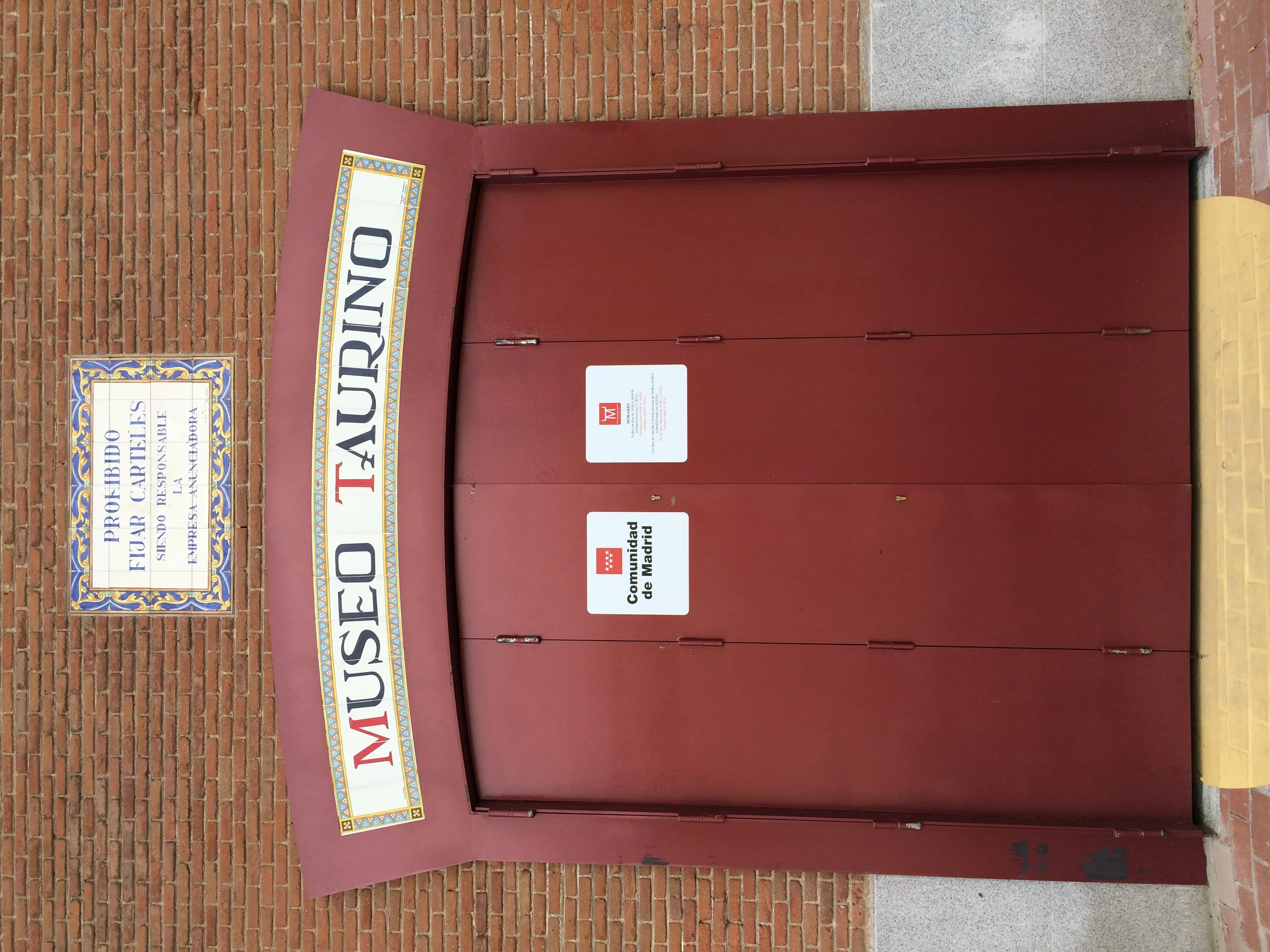 Rode deur met een bord met de tekst 'MUSEO TAURINO' op een bakstenen muur