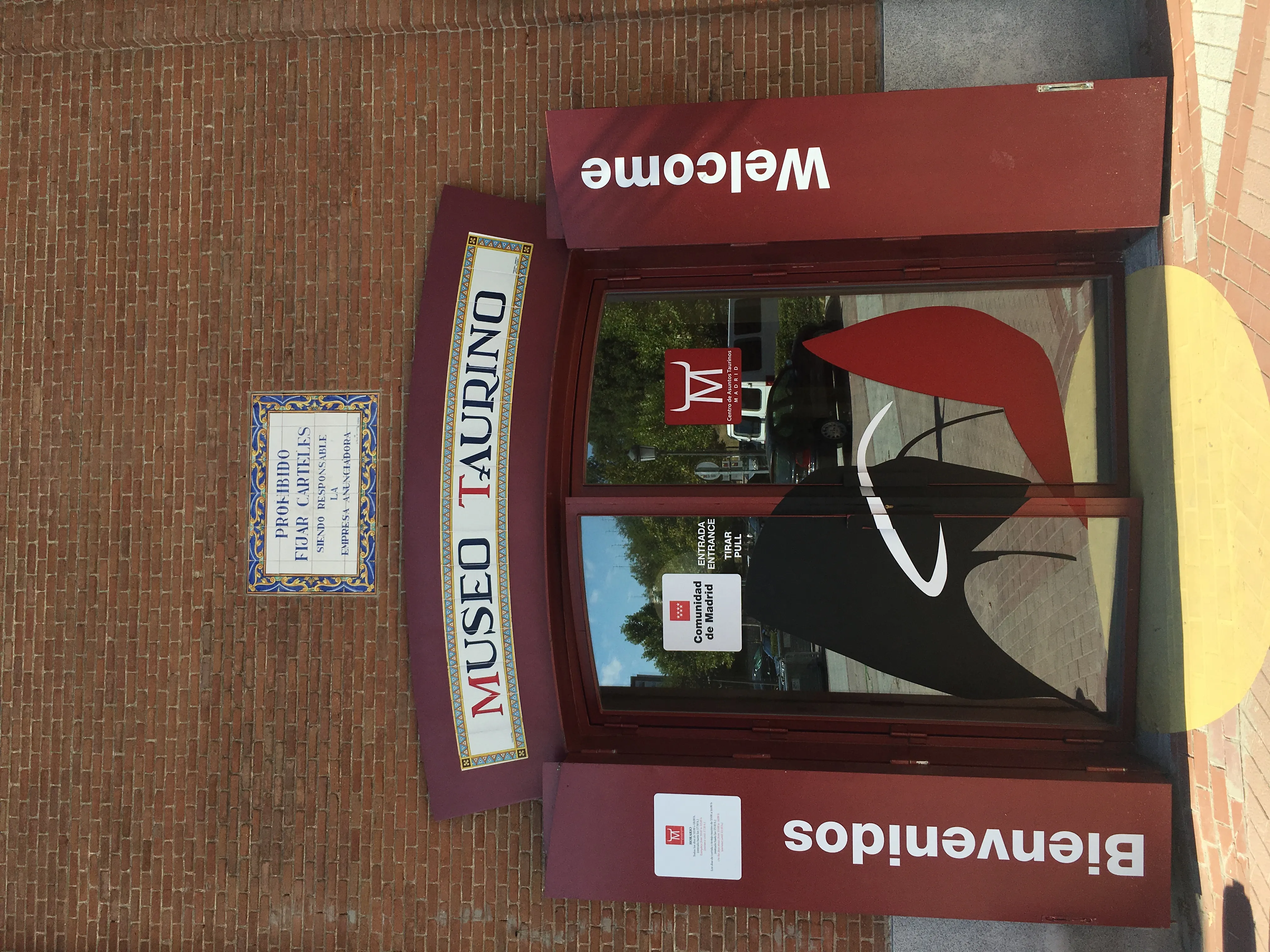 Rood ingangs bord voor het Stierenvechtmuseum met de tekst 'MUSEO TAURINO' en 'Bienvenidos' op een bakstenen muur.