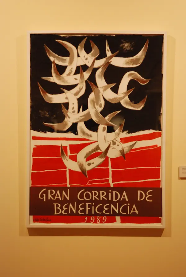 Gelijste poster met stierenhoorns en de tekst 'GRAN CORRIDA DE BENEFICENCIA 1989' aan een muur