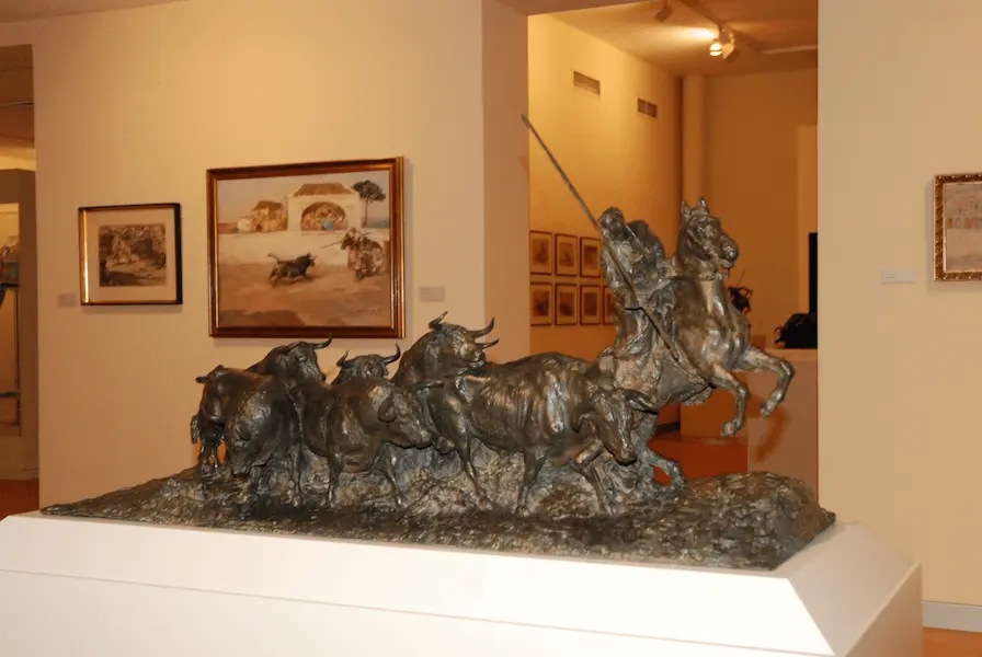 Bronzen beeld van een stierengevechtscène met een matador te paard en aanvallende stieren in een museumgalerij
