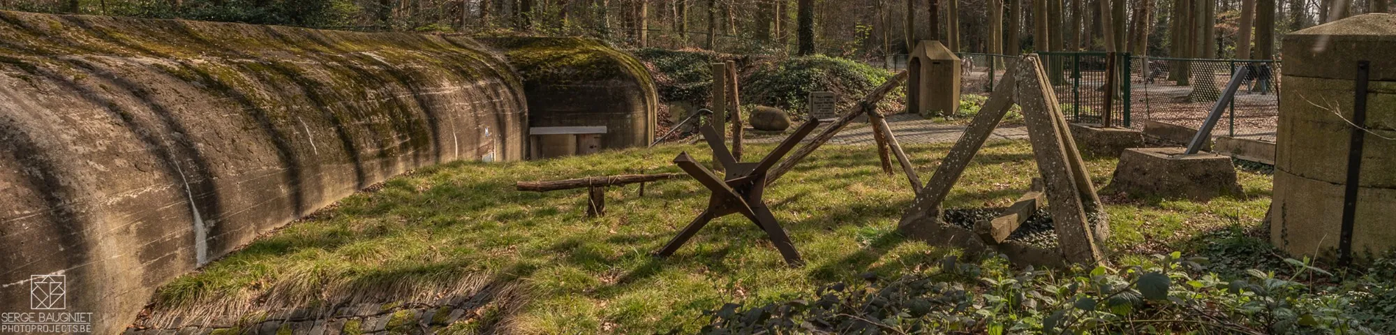 Estructuras de búnkeres de hormigón y obstáculos antitanque tipo 'erizo checo' en una zona boscosa de hierba en un sitio de fortificación preservado de la Segunda Guerra Mundial.