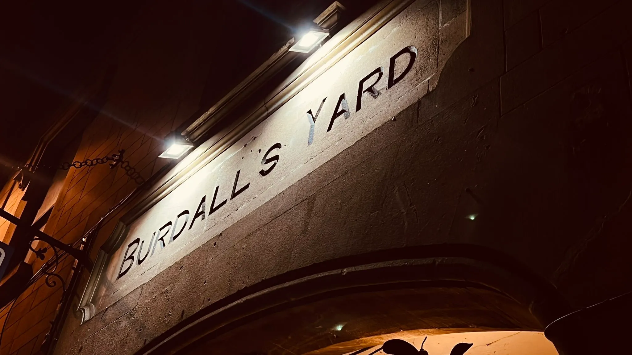 Night view of the entrance and stone frontage of Burdall's Yard in Bath.