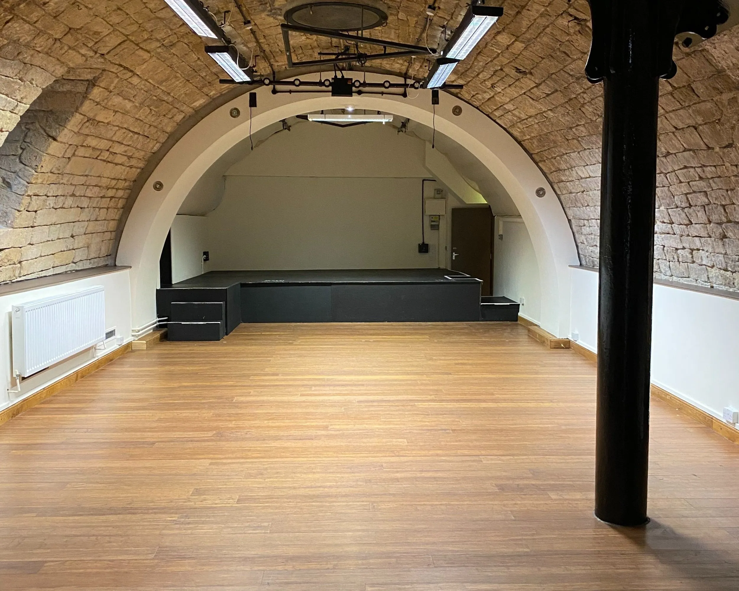 Arched brick performance room inside Burdall's Yard with a stage and seating.
