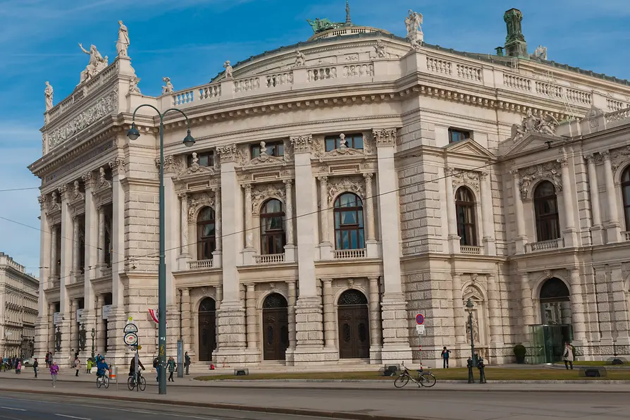 Neoclassicistische gevel van het Burgtheater met stenen zuilen, boogramen en beelden op de daklijn onder een blauwe hemel