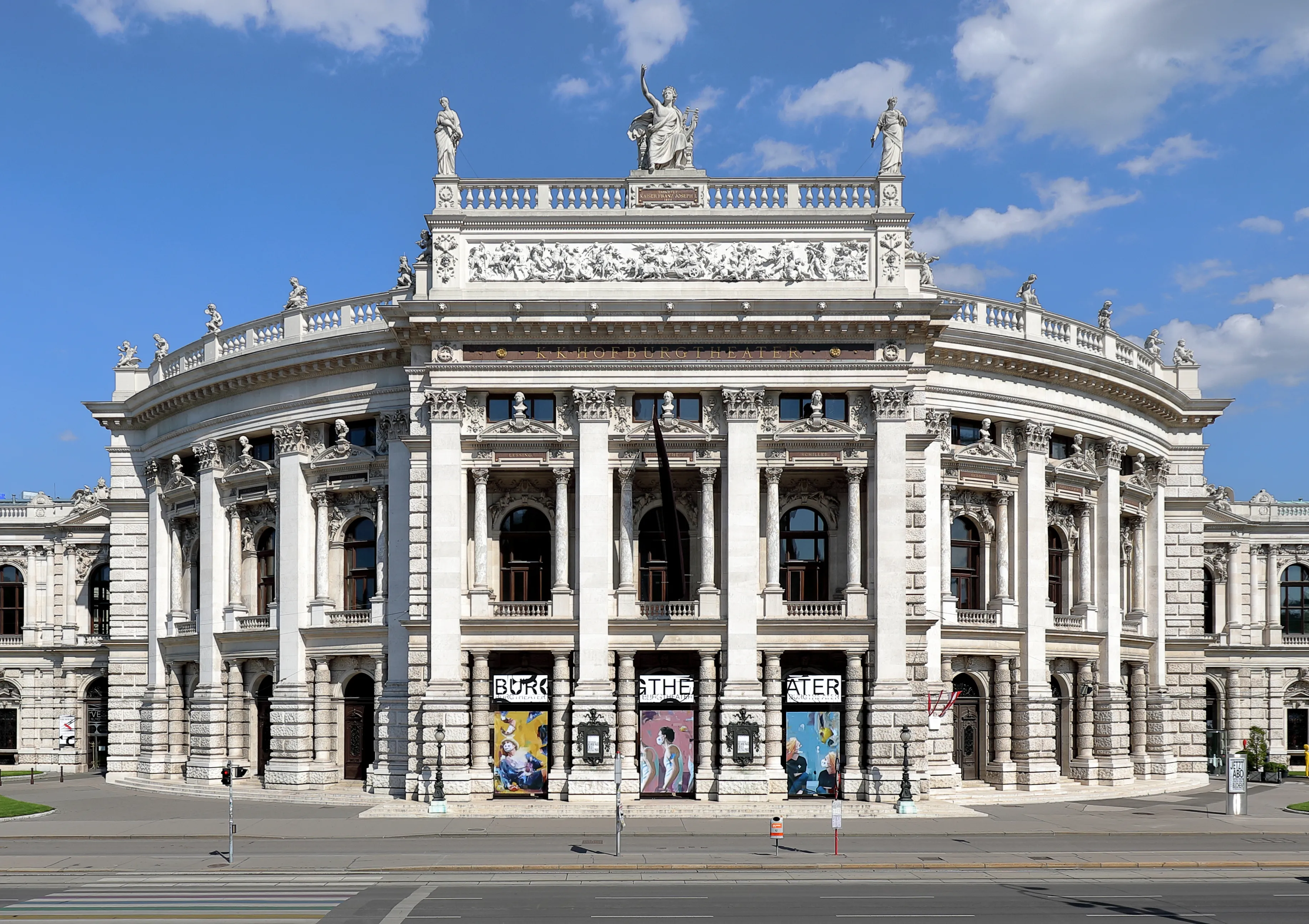 Witte neoklassieke gevel van het Burgtheater in Wenen met zuilen, beelden op de dakrand en boogramen onder een blauwe lucht