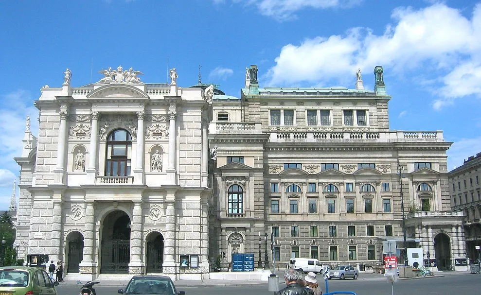 Het Burgtheater gebouw met sierlijke stenen architectuur, boogvormige ingangen en beelden op de daklijn onder een blauwe lucht met wolken.