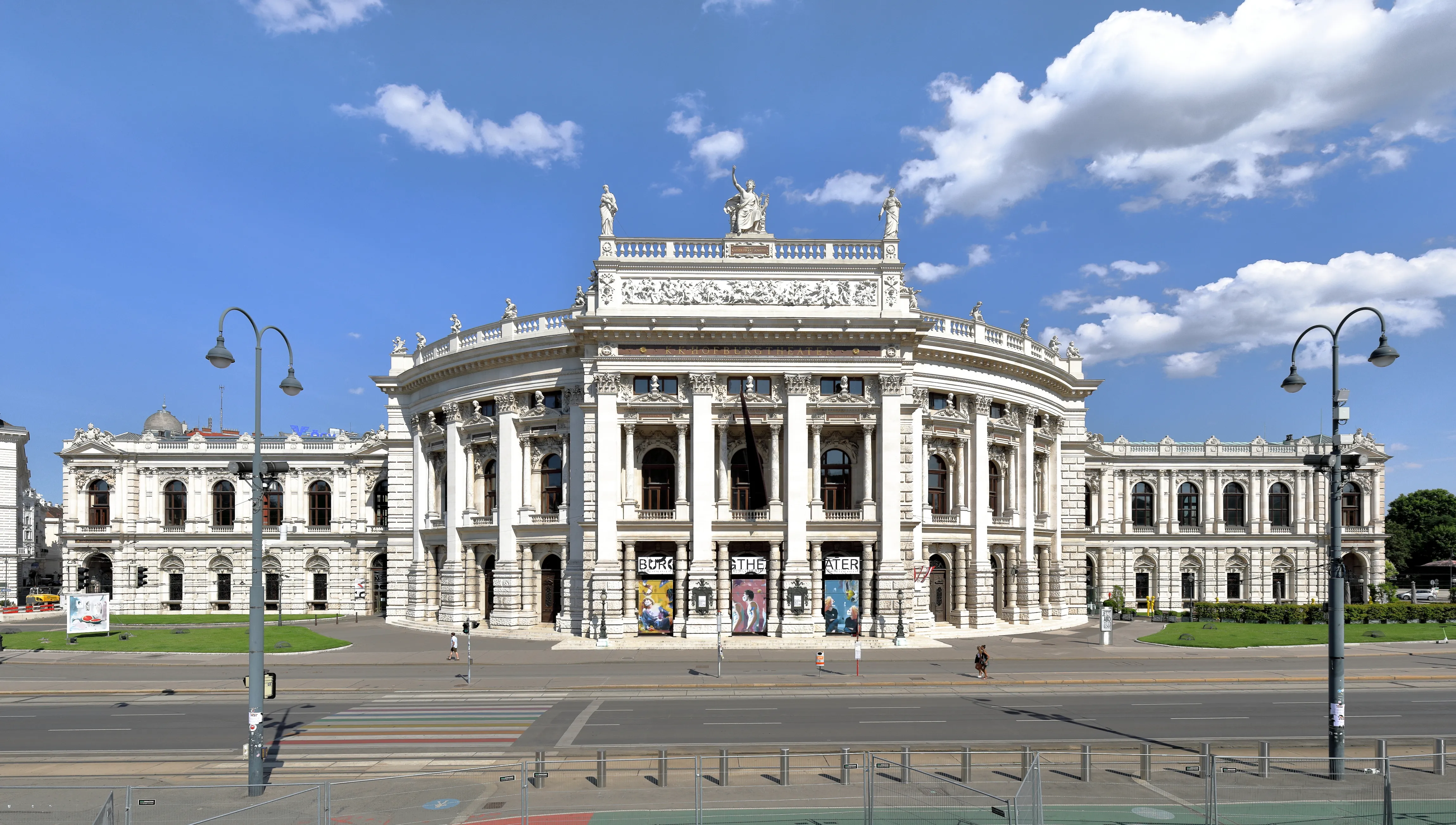 Het Burgtheater, een groot wit neoklassiek gebouw met zuilen en beelden, onder een blauwe hemel met wolken