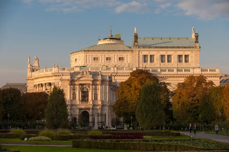 Het Burgtheater-gebouw met zijn neoklassieke gevel, sierlijke details en omringende herfstbomen onder een heldere hemel