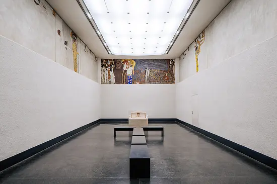 Een lange galerij met een muurschildering op de verste muur en een vitrine in het midden