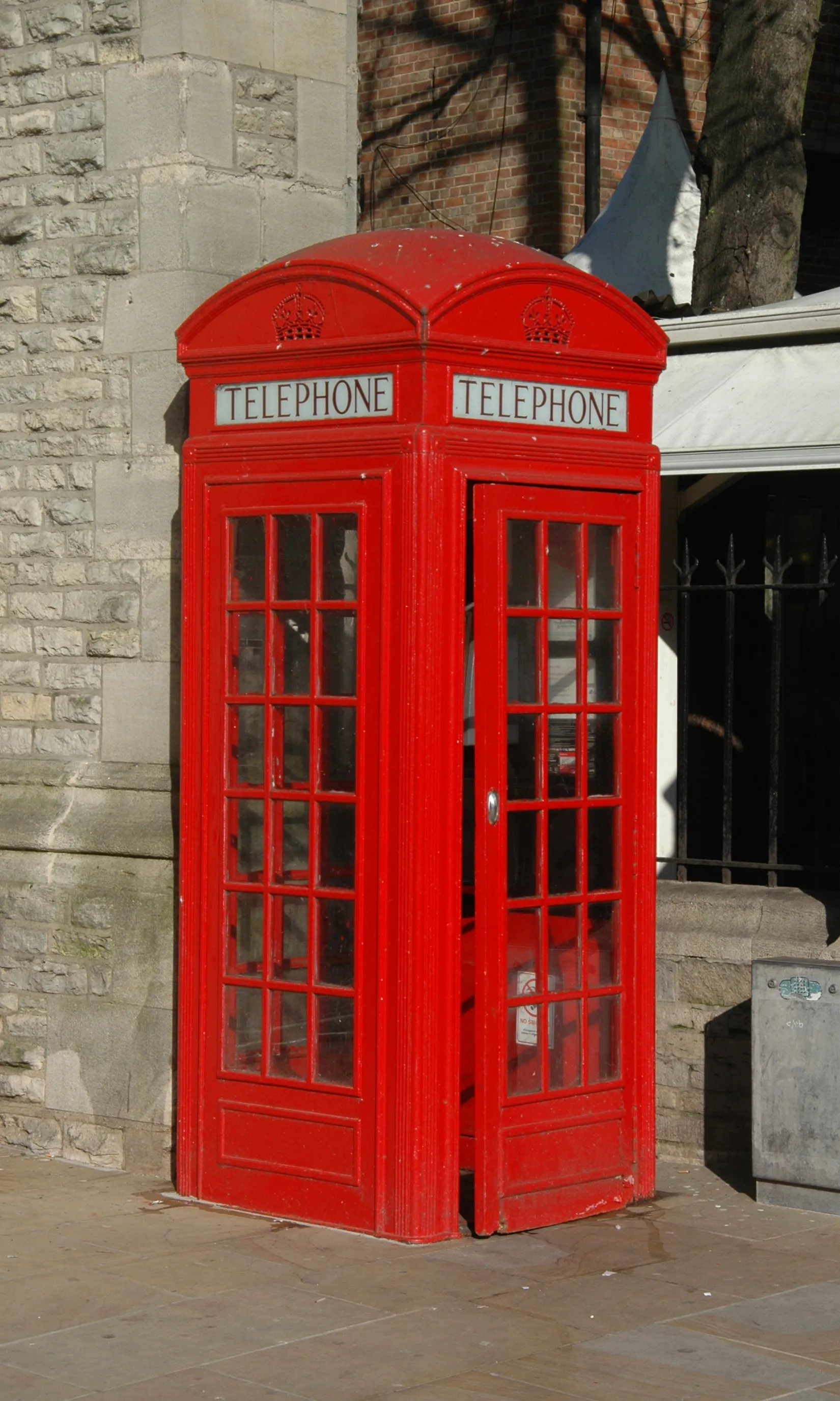 Klassieke rode Britse K2-telefooncel op het trottoir voor een stenen kerkmuur bij de Carfax Tower