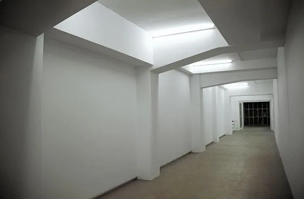 Empty white-walled gallery interior with skylights and concrete floor stretching into the distance