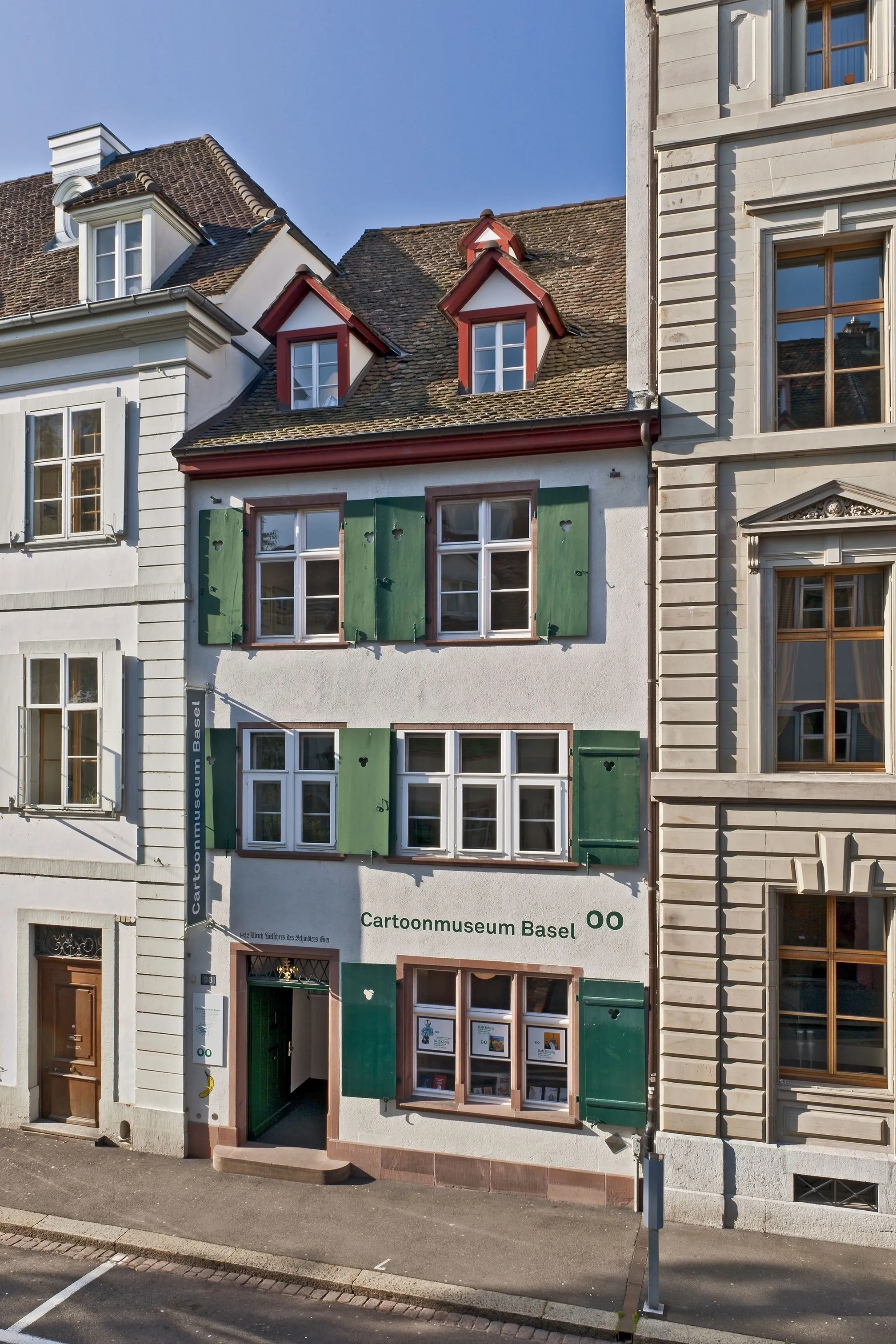 Vista exterior del edificio del Cartoonmuseum Basel con contraventanas verdes y un letrero que dice 'Cartoonmuseum Basel' sobre la entrada