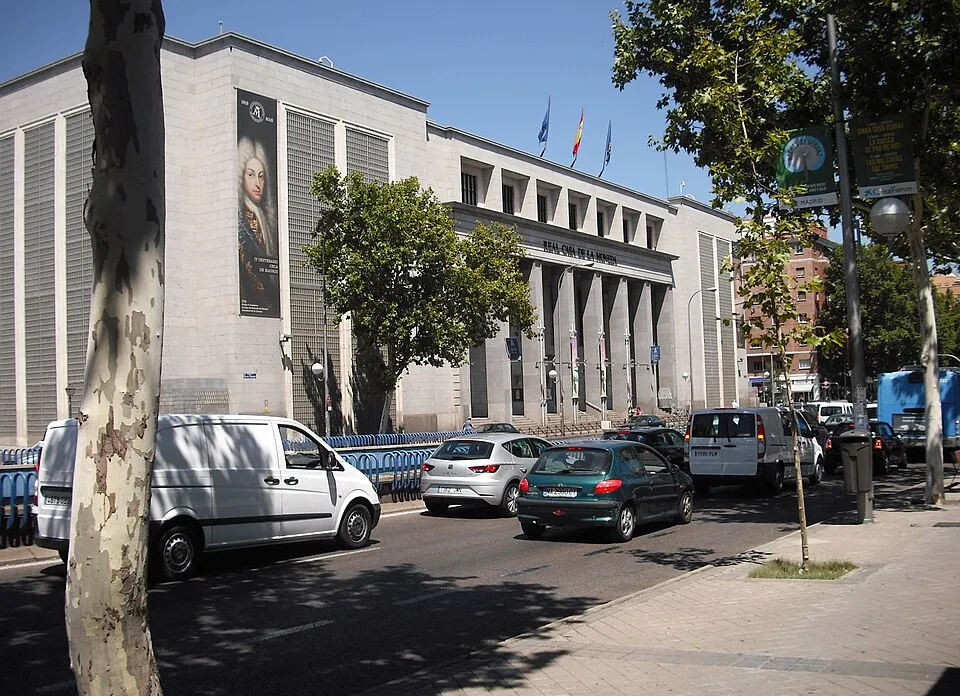 Budynek Museo Casa de la Moneda z dużym banerem portretowym, drzewami i samochodami na ulicy w Madrycie