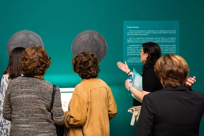 Zwiedzający oglądający duże okrągłe artefakty i panel informacyjny w galerii muzealnej