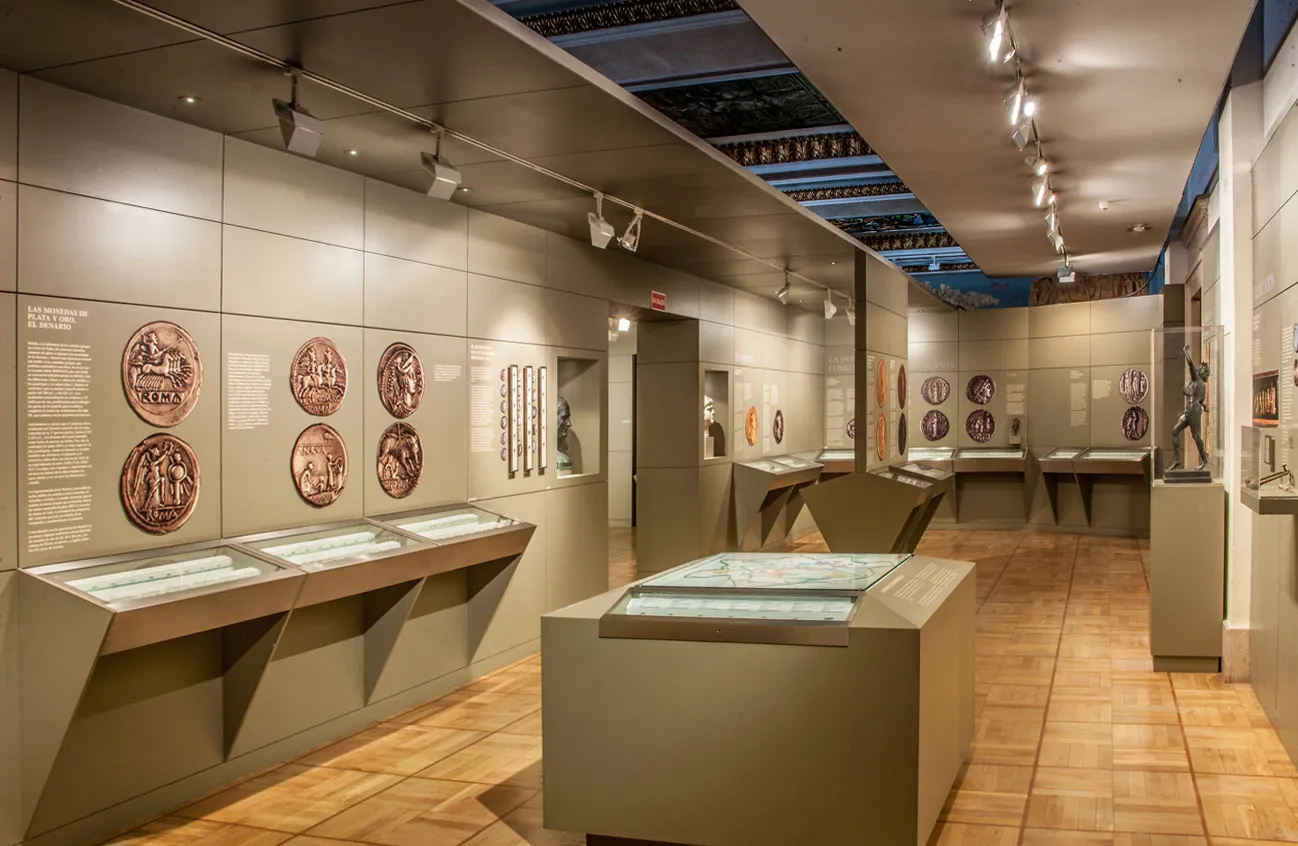 Wnętrze galerii Museo Casa de la Moneda z gablotami i okrągłymi artefaktami na ścianach