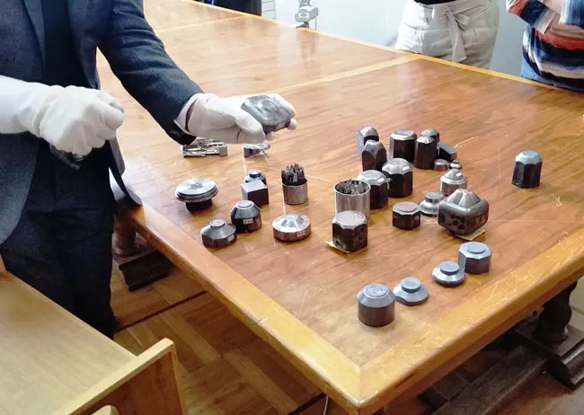 Osoba w białych rękawiczkach trzymająca metalowe formy do monet na drewnianym stole
