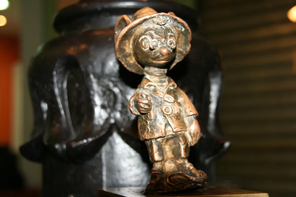 Estatua de bronce de un personaje de ratón con sombrero y abrigo